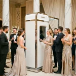 Borne photobooth KRUU installée dans une grande salle de mariage élégante avec des invités en tenue de soirée